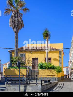 Une maison jaune vif au 11a Calle Adelantado à la Laguna, Tenerife, contraste avec un ciel bleu profond des îles Canaries et des buissons verdoyants dans le jardin. Banque D'Images