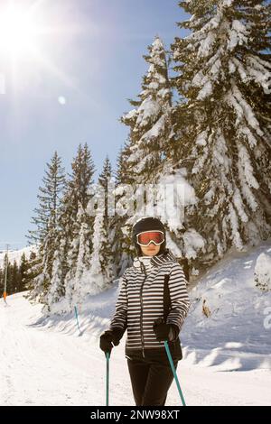 Jeune femme qui profite de la journée d'hiver pour skier sur les pistes enneigées, entourée de grands arbres et habillée pour les températures froides Banque D'Images