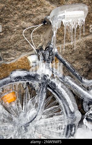 Gros plan vertical d'une bicyclette gelée recouverte de glace qui s'appuie contre un mur de pierre. Un vélo recouvert de glace. Températures glaciales pendant un hiver froid Banque D'Images