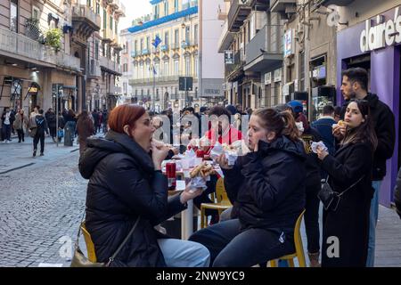 Naples, Italie - 13 février 2023: Les citoyens et les touristes mangent dans la rue, dans le centre-ville, assis aux tables d'un restaurant de restauration rapide. Banque D'Images