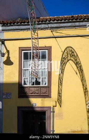 Un fort soleil hivernal projette l’ombre des décorations de Noël sur le mur jaune vif d’un immeuble de la Calle Obispo Rey Redondo, la Laguna Banque D'Images