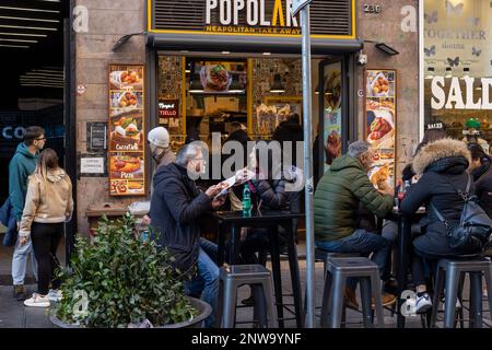 Naples, Italie - 13 février 2023: Les citoyens et les touristes mangent dans la rue, dans le centre-ville, assis aux tables d'un restaurant de restauration rapide. Banque D'Images