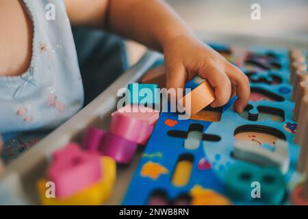 Vue rapprochée des mains de bébé jouant dans un puzzle composé de figurines colorées. Concept d'éducation. Concept d'activité familiale. Concept enfant joyeux Banque D'Images