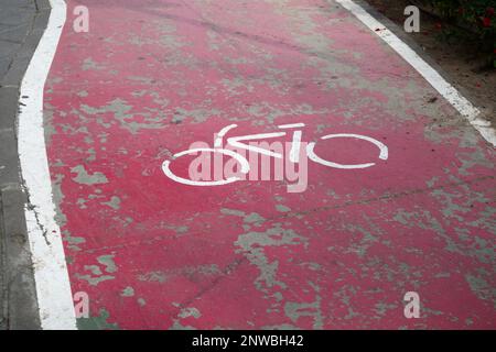 Une piste de vélo rouge et de la peinture usée par le temps dans lequel l'icône d'une bicyclette a été peinte sur l'asphalte indiquant que les véhicules à deux roues comme les vélos Banque D'Images