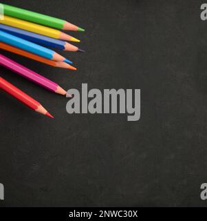 Image de certains crayons de couleur arc-en-ciel sur une surface noire avec un peu de texture et d'espace de copie Banque D'Images