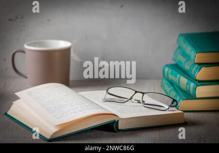 L'atmosphère de l'intimité. Sur le bureau se trouve une pile de livres, de lunettes et un livre ouvert. En arrière-plan se trouve une tasse de thé. La photo est teintée avec sepi Banque D'Images