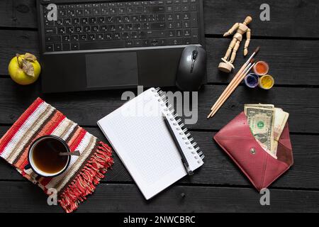 un bloc-notes noir pour ordinateur portable avec de l'argent pour le café se trouve sur la table de travail en bois noir, un ordinateur portable sur la table de travail pendant le travail, processus créatif, indépendant Banque D'Images