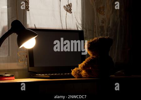 ours en peluche pour enfants assis portant un ordinateur portable sur la table, portant une lampe de table dans les chambres la nuit, portant des fenêtres, solitude, joie dans une la Banque D'Images