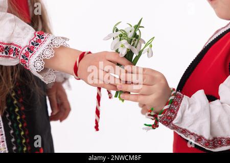 Garçon bulgare enfants, fille en costumes ethniques folkloriques, bouquet de fleurs de printemps neige, laine martenitsa symbole de Mars Baba Marta vacances, Bulgarie Banque D'Images