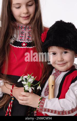 Garçon bulgare enfants, fille en costumes ethniques folkloriques, bouquet de fleurs de printemps neige, laine martenitsa symbole de Mars Baba Marta vacances, Bulgarie Banque D'Images