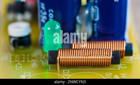 Bobines électromagnétiques, LED verte et composants électroniques sur la carte de circuit imprimé. Gros plan des inductances cylindriques ou de la diode électroluminescente. CI. Banque D'Images