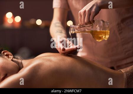 Mains de masseuse appliquant de l'huile naturelle sur le dos de la cliente féminine Banque D'Images