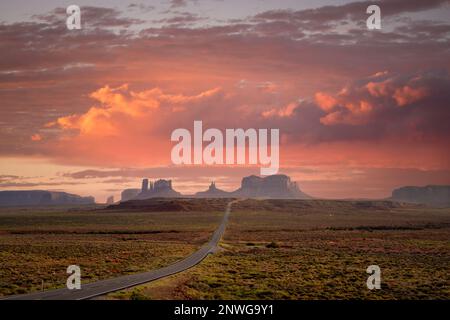 Emblématique Monument Valley en Arizona, Utah pendant l'été, au cours d'un coucher de soleil rose après-midi avec autoroute droite menant à de célèbres formations rocheuses. Banque D'Images