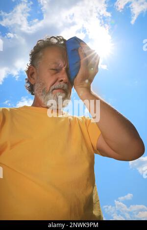 Homme âgé avec pack froid souffrant de coup de chaleur à l'extérieur, vue en angle bas Banque D'Images