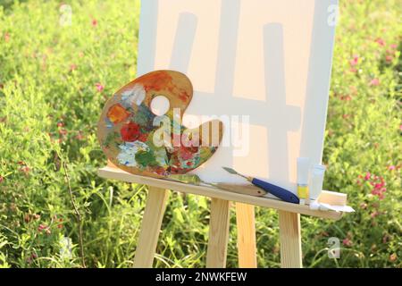 Chevalet en bois avec toile vierge et équipement de peinture dans la prairie. Espace pour le texte Banque D'Images