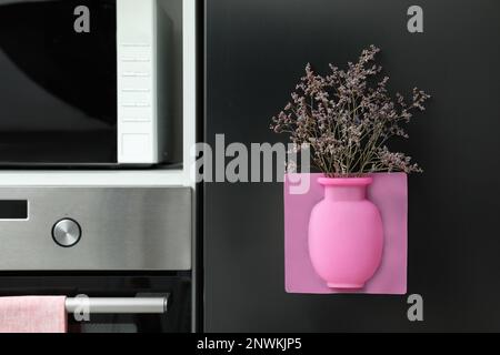 Vase en silicone avec de belles fleurs violettes au réfrigérateur dans la cuisine, espace pour le texte Banque D'Images