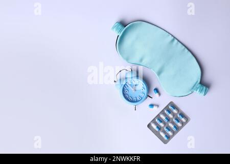 Masque de sommeil, pilules et réveil sur fond blanc, posé à plat. Traitement de l'insomnie Banque D'Images