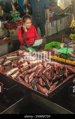 Un poissonnier vend sa prise en parlant sur un smartphone au marché principal de la viande de gros la nuit. Phsar Dumkor, Phnom Penh, Cambodge. © Kraig Lieb Banque D'Images