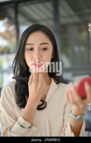 Portrait d'une belle femme asiatique millénaire ou femme d'affaires appliquant un rouge à lèvres, mettant sur son maquillage dans son bureau. Banque D'Images