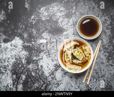 Boulettes asiatiques dans un bouillon, un bol, des baguettes, une sauce soja, un fond de pierre rustique. Vue de dessus. Espace pour le texte. Boulettes chinoises pour le dîner. Gros plan. Banque D'Images