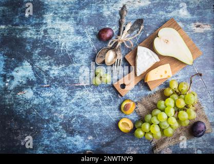 Poire mûre fraîche, plateau de fromages variés, raisins, prunes dans un bol, fond rustique en bois bleu. Espace pour le texte. Vue de dessus. Fruits, Camembert Banque D'Images