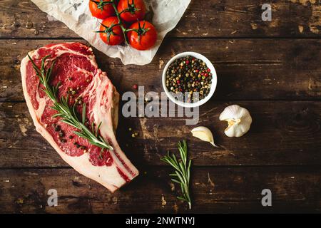 Steak de viande marbré cru, poivre, herbes, tomates, vieux fond de table en bois. Steak de bœuf à l'œil de bœuf prêt à cuire. Vue de dessus. Ingrédients prêts pour Banque D'Images