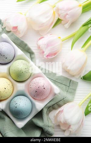 Porte-oeufs de Pâques peint couleurs pastel et tulipes roses sur fond blanc en bois. Vue de dessus. Espace pour le texte. Banque D'Images