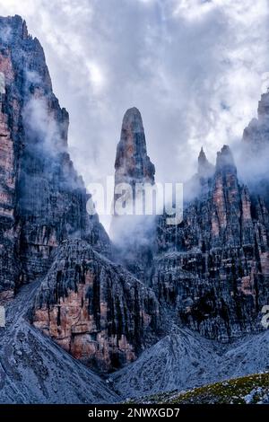 Le sommet de l'aiguille de pierre Campanile Basso à Brenta Dolomites au milieu des falaises rocheuses environnantes, partiellement couvertes de nuages. Banque D'Images