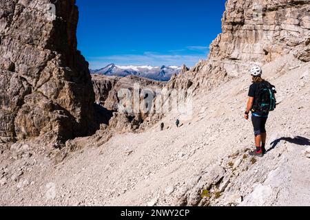 Un grimpeur regarde deux autres sur la via ferrata Sentiero Alfredo Benini, qui fait partie de la via delle Bocchette, le groupe de montagne Adamello au loin. Banque D'Images