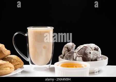 Thé avec du lait dans une tasse en verre avec un double fond et des gâteaux sur fond noir, placer pour le texte Banque D'Images