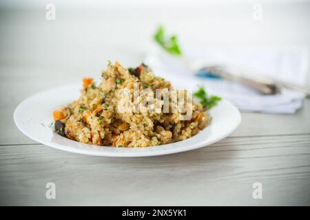 boulgour cuit avec des légumes, des carottes et des champignons séchés dans une assiette sur une table en bois. Banque D'Images
