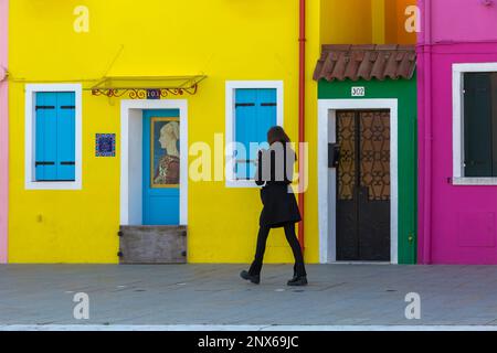 Femme tenant un appareil-photo marchant devant des maisons aux couleurs vives à Burano, Venise, Italie en février Banque D'Images