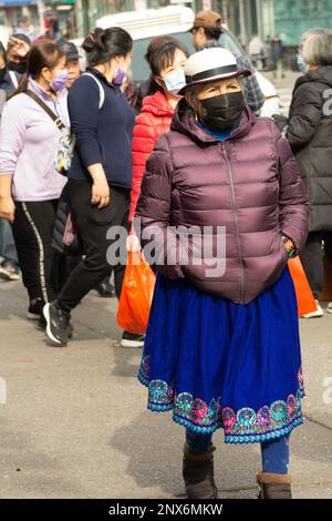 Une femme sud-américaine portant une jupe et un chapeau traditionnels et un masque marche sur main St dans Chinatown, Flushing, Queens, New York City. Banque D'Images