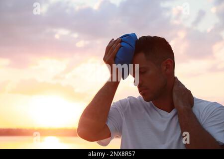 Homme avec pack froid souffrant de coup de chaleur près de la rivière au coucher du soleil Banque D'Images