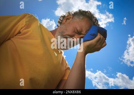 Homme âgé avec pack froid souffrant de coup de chaleur à l'extérieur, vue en angle bas Banque D'Images