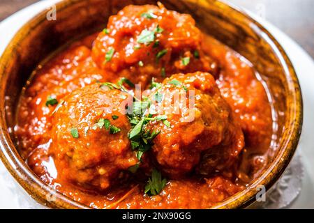Cuisine espagnole des boulettes de viande maison traditionnelles dans une riche sauce tomate servies avec du basilic frais - tapas dans un plat rustique en terre cuite. Banque D'Images
