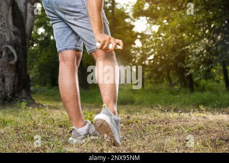 Homme appliquant un insectifuge sur la jambe dans le parc, gros plan. Prévention des piqûres de tiques Banque D'Images