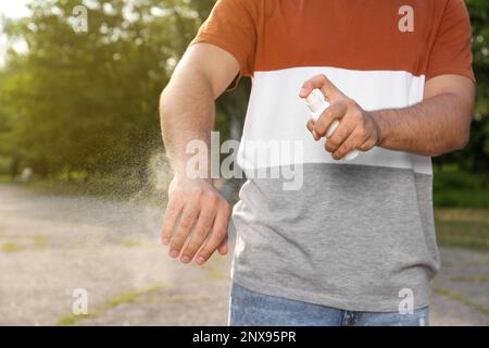 Homme appliquant un insectifuge sur le bras dans le parc, gros plan. Prévention des piqûres de tiques Banque D'Images