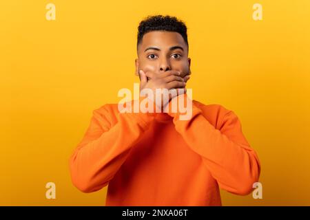 Homme choqué sérieux tenant les mains sur la bouche et regardant la caméra, choqué bemused avec les nouvelles. Studio d'intérieur isolé sur fond jaune Banque D'Images