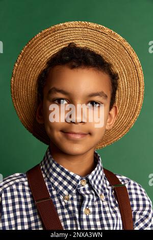 Joli petit garçon, enfant en chemise à carreaux et short suspendu isolé sur fond vert foncé. Concept d'enfance, amitié, rétro Banque D'Images