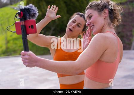 Deux jeunes femmes caucasiennes enregistrent une vidéo avec un smartphone agitant Banque D'Images