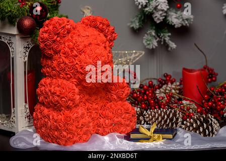 Gros plan d'un ours en peluche rouge fait de roses sur une table à côté d'un assortiment de décorations de Noël Banque D'Images