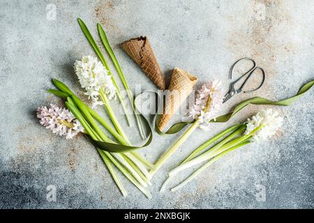 Arrangement de printemps avec des fleurs de jacinthe roses et blanches, des cornets de gaufres, du ruban et des ciseaux sur une table Banque D'Images