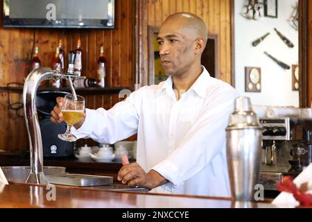 Le barman noir verse de la bière au bar de la station touristique Banque D'Images