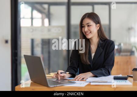 Femme d'affaires asiatique utilisant une calculatrice et un ordinateur portable pour faire des finances mathématiques sur un bureau, impôts, rapports, comptabilité, statistiques, et analytique Banque D'Images