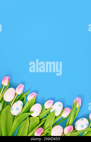 Fleurs de printemps de tulipe blanches avec bouts roses et oeufs de pâques sur le côté de fond bleu avec espace de copie Banque D'Images