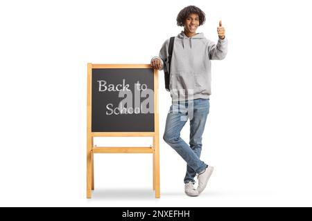 Afro-américain étudiant penché sur un tableau noir avec le texte de retour à l'école et gestantes pouces vers le haut isolés sur fond blanc Banque D'Images