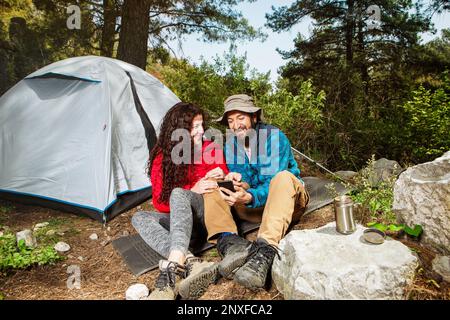 Jeunes touristes couple voyageurs avec abri de tente assis dans la nature, en utilisant le smartphone Banque D'Images