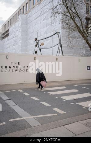 L'ancienne ambassade américaine étant réintégrée dans une propriété de luxe à l'arrière-plan, une femme qui est pendue traverse la route sur une traversée de zébrée à Grosvenor Square à Mayfair, le 27th février 2023, à Londres, en Angleterre. La chancellerie Rosewood, en partenariat avec le promoteur immobilier Qatari Diar, ouvrira ses portes en 2024 à l'emplacement de l'ancien américain classé de catégorie II Bâtiment de l'ambassade. Banque D'Images