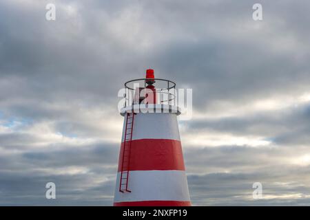 Top of a red and white lighthouse beacon against a cloudy sky. Stock Photo